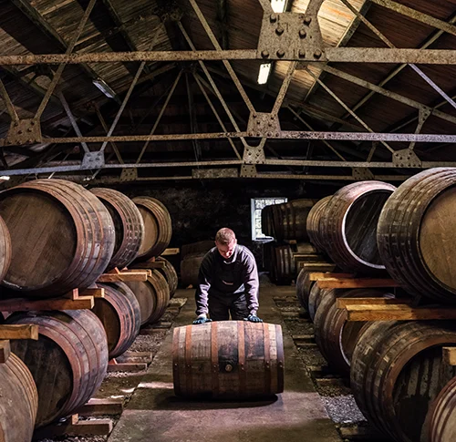 A person rolling a barrel in a distillery